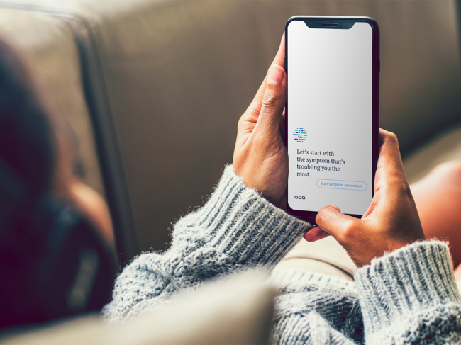 Person on couch using Ada symptom checker app on smartphone