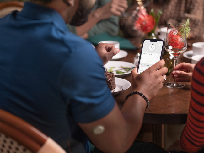 Person wearing G7 sensor on arm checks app before eating