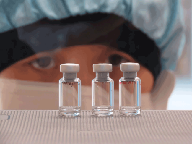 Researcher in PPE looking at three vials