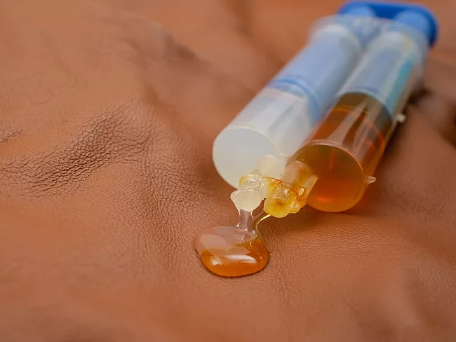 Double syringe with epoxy gel glue spilling on brown leather