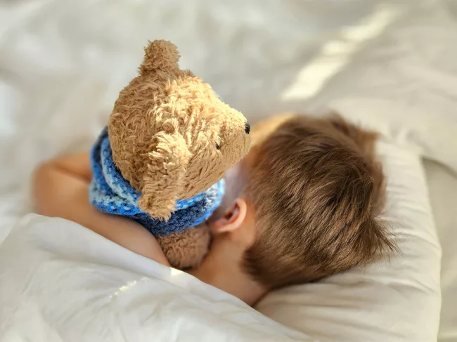 Photo of child in bed hugging teddy bear