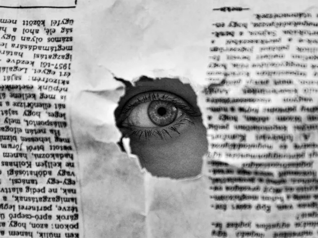Eye looking through a hole in a article paper