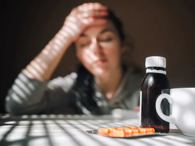 Female holding head with medicine on table