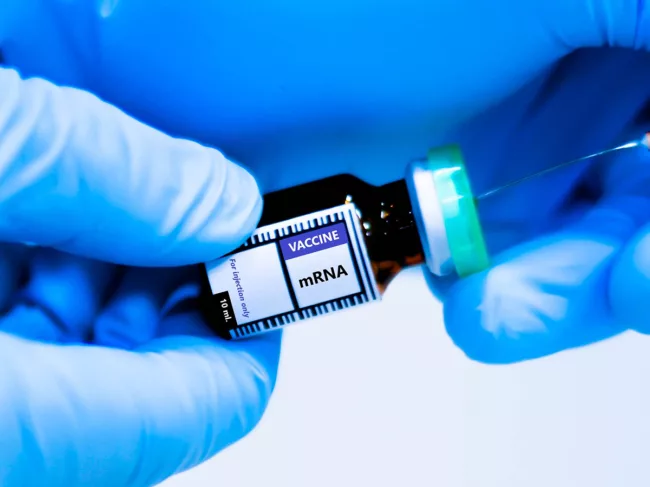 Gloved hands holding mRNA vaccine vial