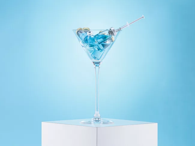 Vaccine vials and syringe in a martini glass.