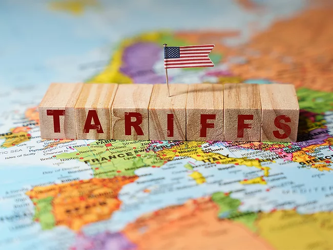 Wooden blocks spelling TARIFFS with a U.S. flag on top, placed on a map of Europe