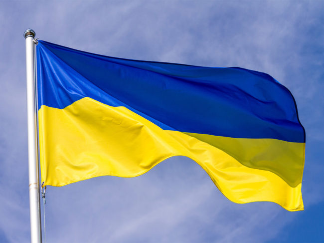 Flag of Ukraine waving in the wind on flagpole against the sky