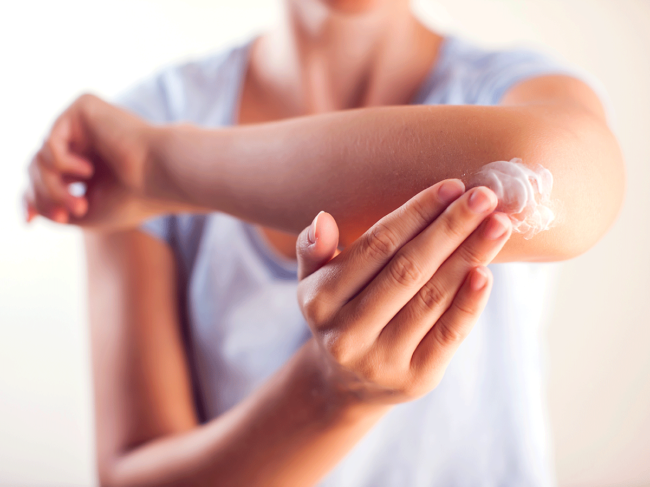 Woman applying skin cream to elbow