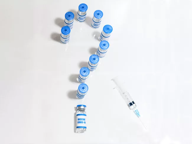 Syringe and COVID-19 vaccine vials as question mark