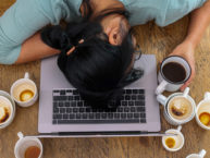 Photo of woman sleeping on laptop surrounded by coffee mugs