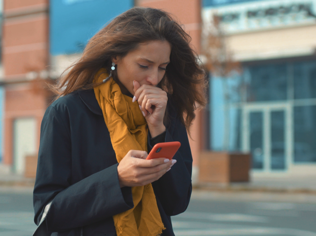 Woman holding smartphone coughing