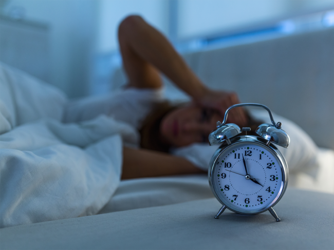 Clock with woman awake in bed in background