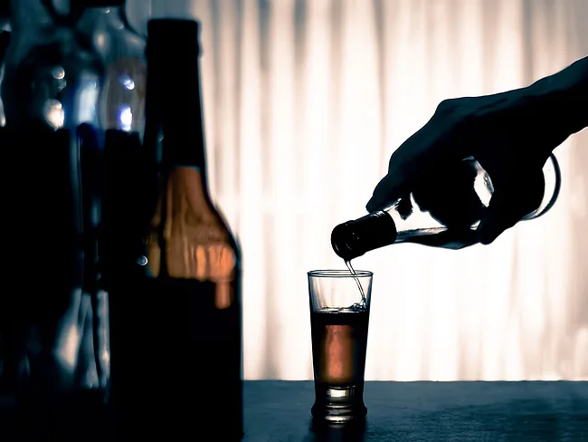 Bottles of alcohol with hand pouring into glass